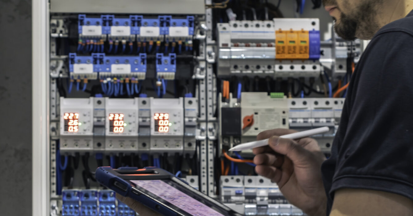 man-electrical-working-switchboard-with-fuses-uses-tablet