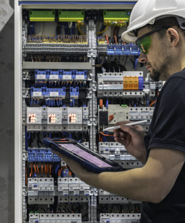 man-electrical-working-switchboard-with-fuses-uses-tablet